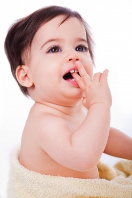 A baby wrapped in a towel is smiling and touching their mouth with fingers on a plain white background.