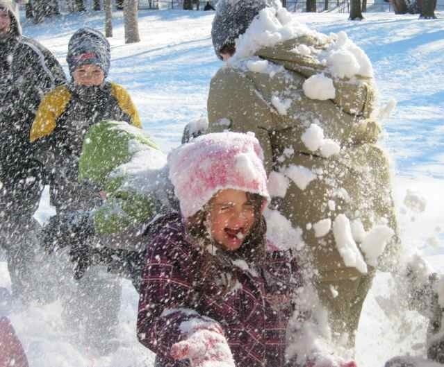 Children playing joyfully in snow, bundled in colorful winter clothing, as snow scatters around them, creating a fun and lively scene outdoors.
