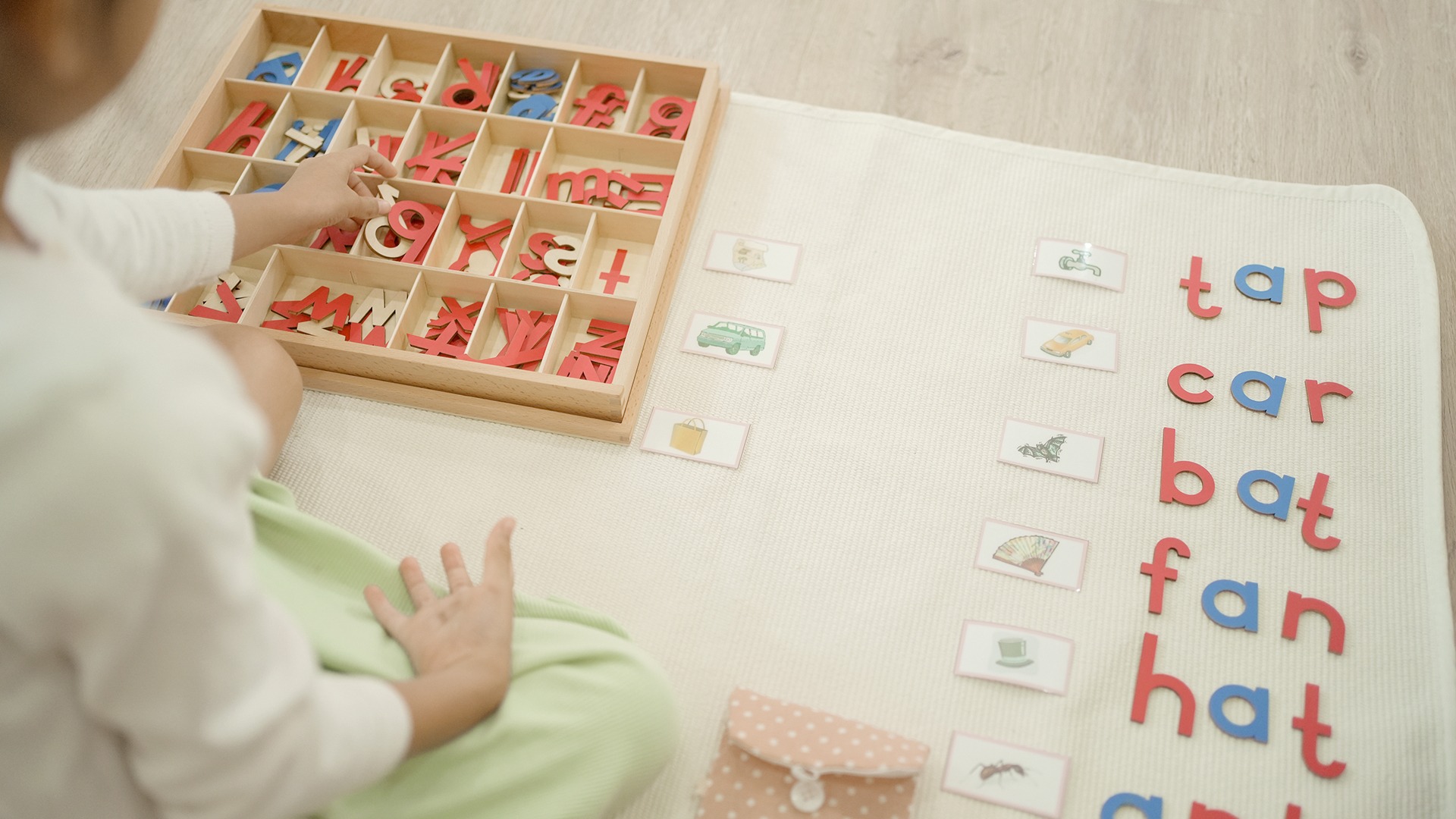 A person arranges colorful wooden letters on a mat, matching words with pictures, enhancing learning through engaging educational activities.