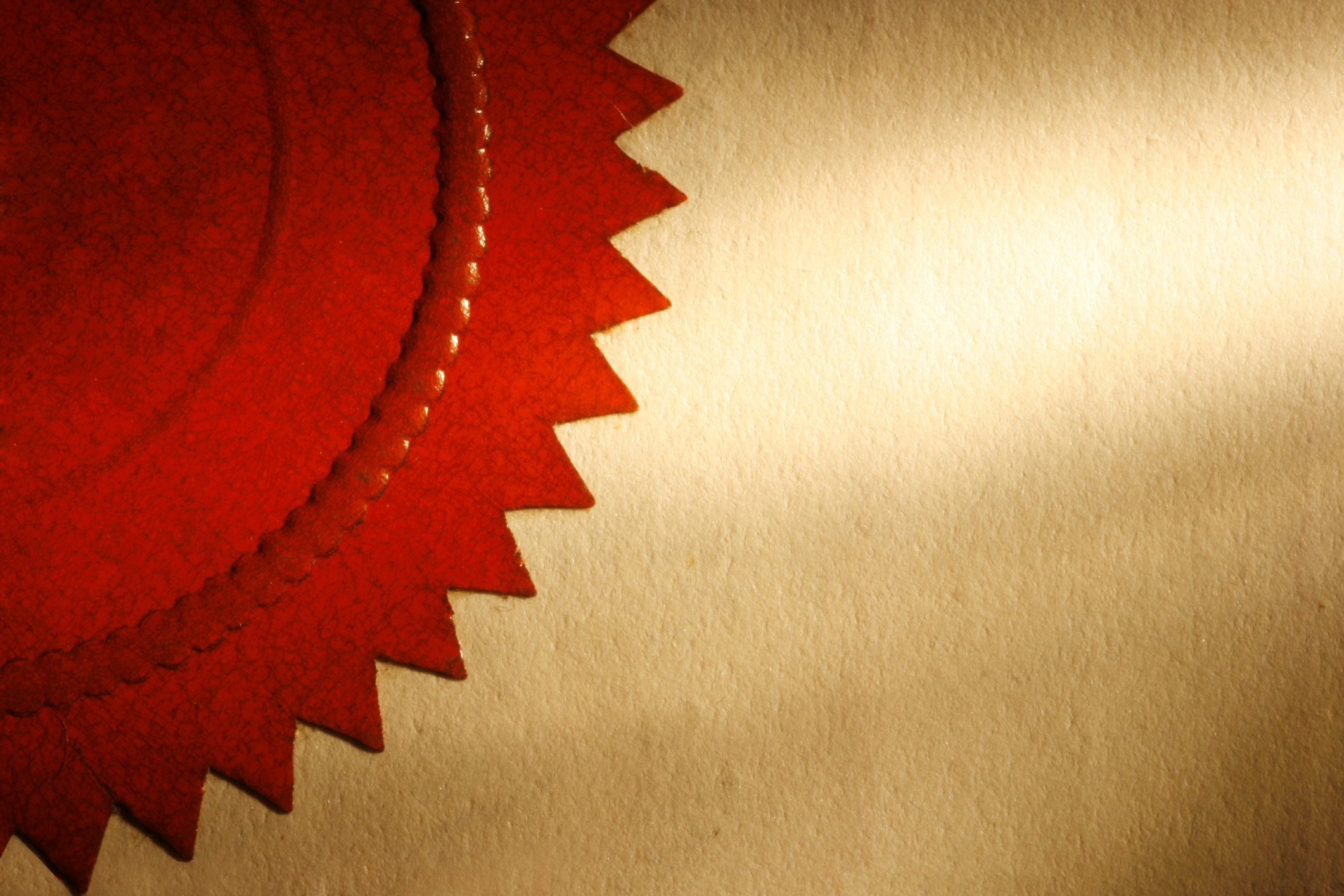 A red, embossed seal with a zigzag edge on textured, tan paper, suggestive of a diploma or official document.