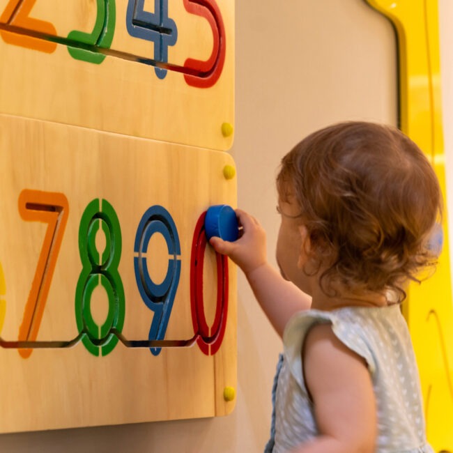 A child interacts with a colorful wooden puzzle featuring numbers, focusing on problem-solving and tactile learning in an engaging educational environment.