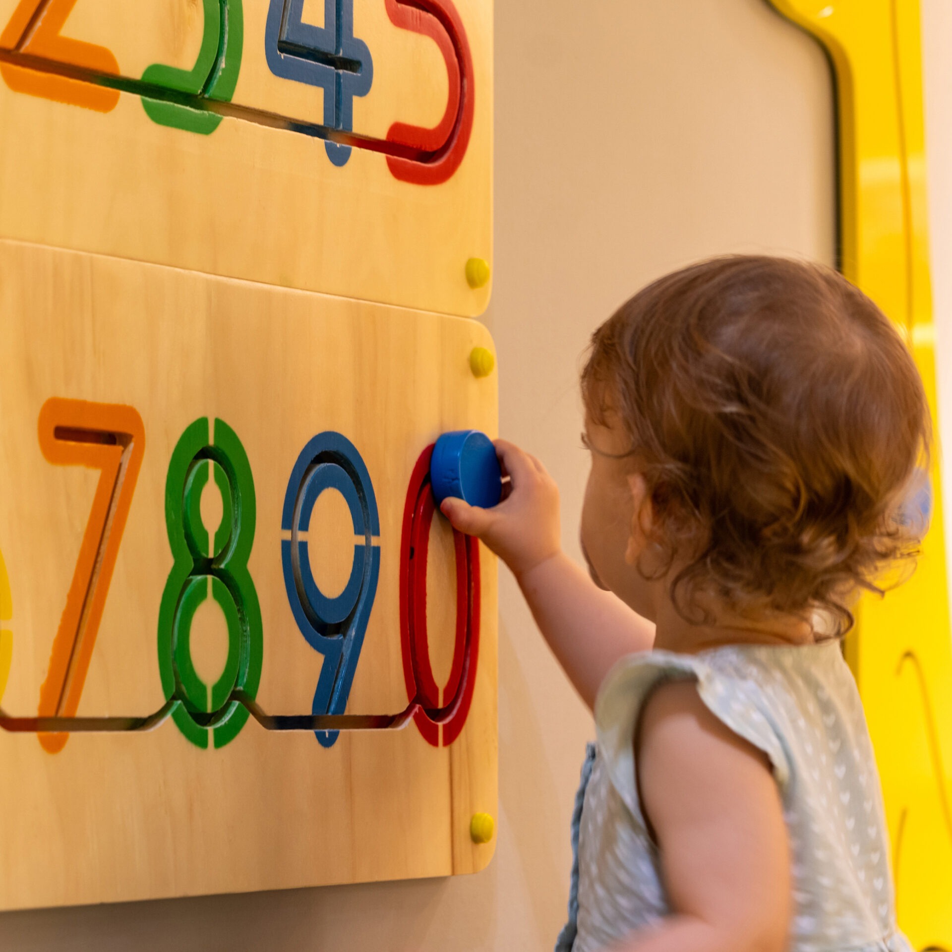 A child interacts with a colorful wooden puzzle featuring numbers, focusing on problem-solving and tactile learning in an engaging educational environment.
