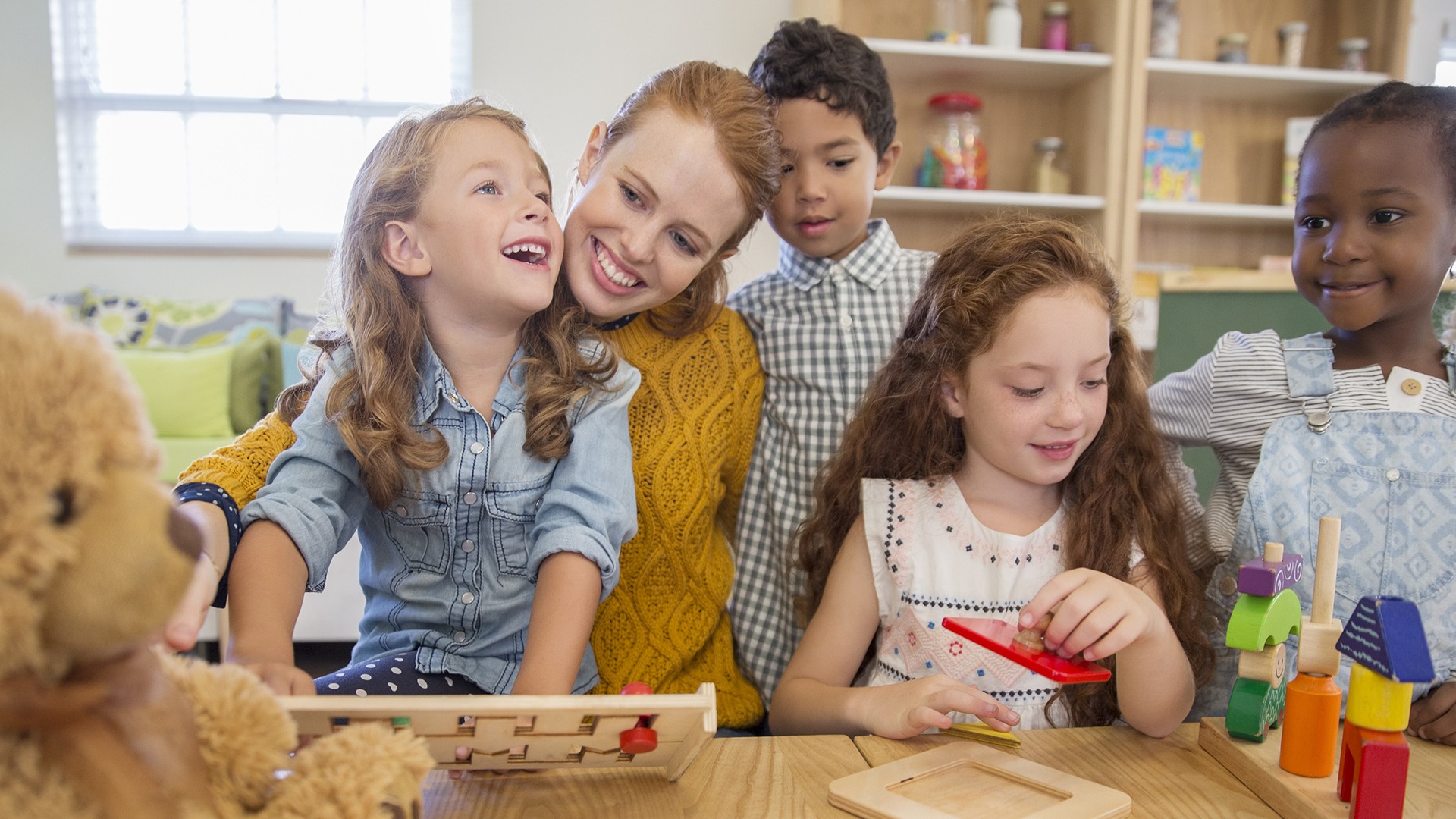 A person and four children engage with educational toys in a bright, inviting classroom setting, fostering learning and joy.