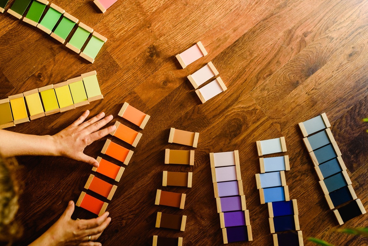 A person arranges colorful paint swatches on a wooden table, creating a visually appealing pattern with a spectrum of hues.