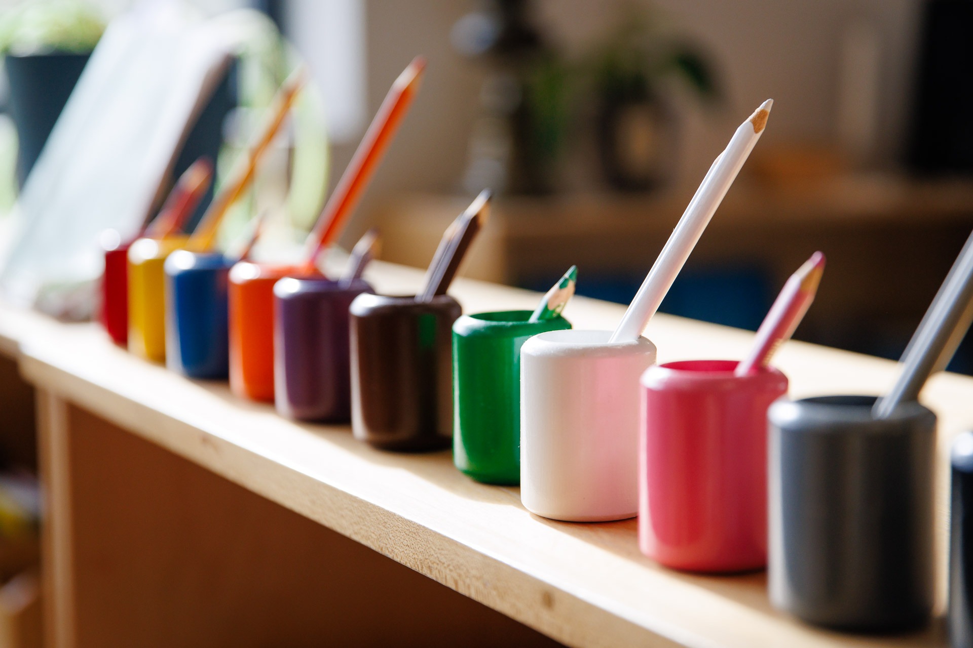 Colorful pencils in matching holders on a wooden shelf, creating a vibrant and organized art setup in a softly lit room.