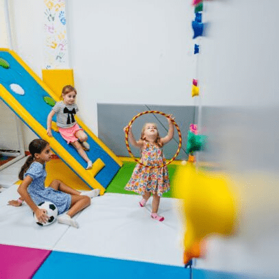 Children playing in an indoor playground with a short climbing wall in the right foreground.